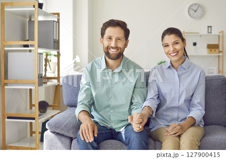Young happy married couple sitting on the sofa in the living room at home and smiling. 127900415