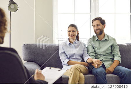 Happy smiling young couple sitting on couch at counselor's office, listening advices and smiling. 127900416
