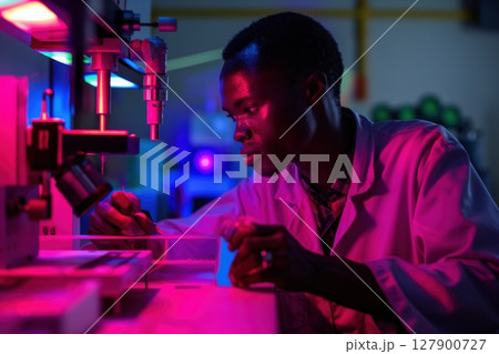Young scientist is conducting research in a laboratory, illuminated by vibrant neon lights, highlighting the cutting edge technology and his focused expression 127900727