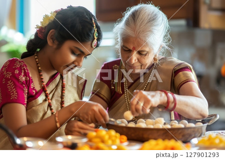 Indian grandmother and her granddaughter wearing traditional clothing preparing food in the kitchen 127901293
