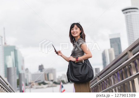 Happy young southeast asian woman teenager blogger using smartphone searching travel guide. World travel explorer tourism concept local cultural experience in Bangkok Asia near Chao Phraya river Happy young southeast asian woman teenager blogger using smartphone searching travel guide. World travel explorer tourism concept local cultural experience in Bangkok Asia near Chao Phraya river 127901389