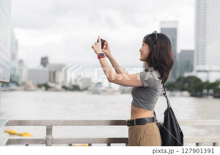 Happy solo southeast asian woman teenager blogger world travel explorer express boat wait to take photo with smartphone Chao Phraya River Bangkok. Asia tourism local cultural experience concept Happy solo southeast asian woman teenager blogger world travel explorer express boat wait to take photo with smartphone Chao Phraya River Bangkok. Asia tourism local cultural experience concept 127901391