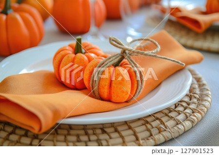Two small pumpkins tied with twine are laying on an orange napkin on a plate, creating a warm and inviting thanksgiving table setting 127901523