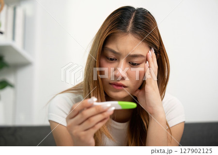 Emotional Reaction to Pregnancy Test Result. A young woman looks worried while checking a pregnancy test. 127902125
