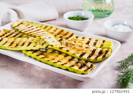 Grilled zucchini slices on a plate with sauce and herbs on the table 127902491