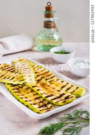 Grilled zucchini slices on a plate with sauce and herbs on the table vertical view 127902493