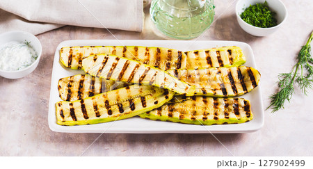 Grilled zucchini slices on a plate with sauce and herbs on the table web banner 127902499