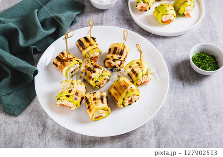 Grilled zucchini rolls filled with cream cheese and tomatoes on a plate on the table 127902513