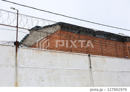 High Brick Wall with Barbed Wire Surrounding a Prison: A Symbol of Confinement and Security 127902979
