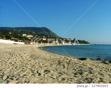Beautiful view of the sea coast in Calabria, showcasing crystal-clear blue waters gently meeting the rugged shoreline. The vibrant coastline is framed by rocky cliffs and lush greenery, highlighting 127903045