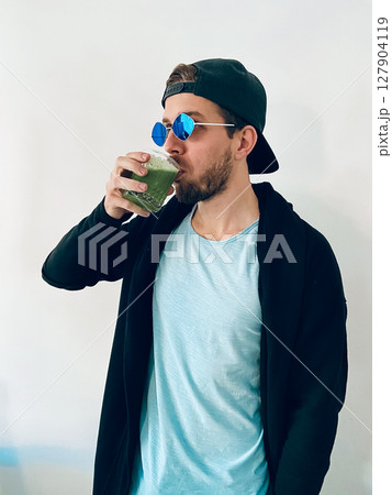 A Young Man Wearing Stylish Sunglasses is Enjoying a Refreshing Green Smoothie With Pleasure 127904119