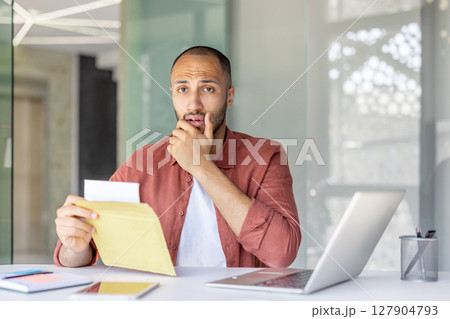 Portrait of upset worried man inside office, employee received letter with bad and sad news in mail. Businessman holding envelope with notification and looking at camera. Portrait of upset worried man inside office, employee received letter with bad and sad news in mail. Businessman holding envelope with notification and looking at camera. 127904793