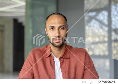 A portrait of a young man with a short haircut and a red shirt, looking directly at the camera. A portrait of a young man with a short haircut and a red shirt, looking directly at the camera. 127905024