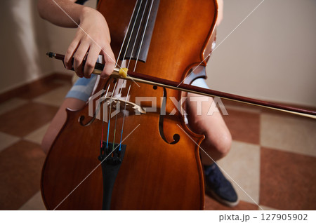 A detailed view of a cello being played by a student, showing hand positioning and technique, emphasizing music education and the beauty of classical instruments in practice. 127905902