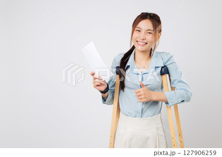 Broken leg or foot woman with crutches holds bill payment paper, recovering from accident and leaning on crutches during her healing journey. isolated studio white background 127906259