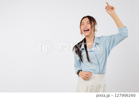 Happy young Asian woman dancing and listening music with headphones and raised hands while enjoying lifestyle full of smile, joy, People emotions, and music. isolated studio white background 127906260