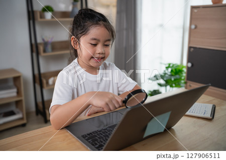 Young girl using magnifying glass while studying on laptop at home, focused on learning and exploring, indoor educational environment for children Young girl using magnifying glass while studying on laptop at home, focused on learning and exploring, indoor educational environment for children 127906511