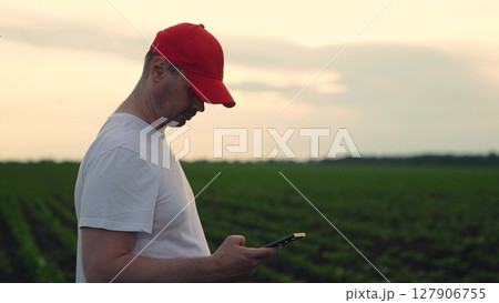 Agriculture, Farmer using smartphone in the field, Modern agriculture technology, Man in red cap on farmland, Rural man checking phone, Fieldworker with device outdoors, Monitoring crops with Agriculture, Farmer using smartphone in the field, Modern agriculture technology, Man in red cap on farmland, Rural man checking phone, Fieldworker with device outdoors, Monitoring crops with 127906755