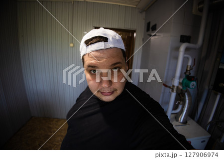 Technician wearing a white cap inspecting a heating system in a boiler room, ensuring optimal operation and thorough maintenance for safety and energy efficiency. 127906974