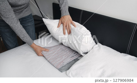 man puts his pajamas under his pillow 127906984