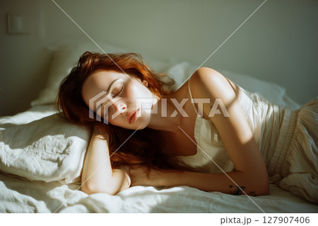 A woman with long red hair is laying on a bed 127907406