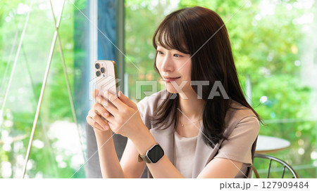 カフェでスマートフォンを使う笑顔の女性 127909484
