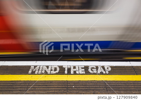 Blurry London Underground Train Passes MIND THE GAP Warning on Platform Edge, UK Transit Safety 127909840
