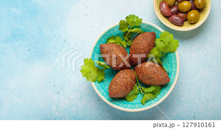 Delicious middle eastern kibbeh on blue ceramic plate top view on light beige background Delicious middle eastern kibbeh on blue ceramic plate top view on light beige background 127910161