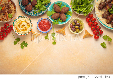 Top view of a vibrant table filled with lebanese dishes and mezze, featuring meat kebabs, falafel, kibbeh, hummus, sambousek, rice, olives. Middle eastern or Arab dishes, space for text 127910163