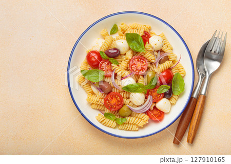 Italian pasta salad with fusilli, cherry tomatoes, mozzarella, olives, basil on beige background top view, Italian cuisine 127910165