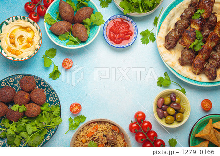 Top view of a vibrant table filled with lebanese dishes and mezze, featuring meat kebabs, falafel, kibbeh, hummus, sambousek, rice, olives. Middle eastern or Arab dishes, space for text 127910166