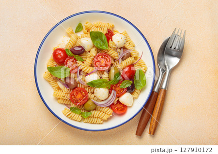 Italian pasta salad with fusilli, cherry tomatoes, mozzarella, olives, basil on beige background top view, Italian cuisine 127910172