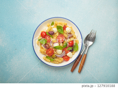 Italian pasta salad with fusilli, cherry tomatoes, mozzarella, olives, basil on blue background top view, Italian cuisine Italian pasta salad with fusilli, cherry tomatoes, mozzarella, olives, basil on blue background top view, Italian cuisine 127910188