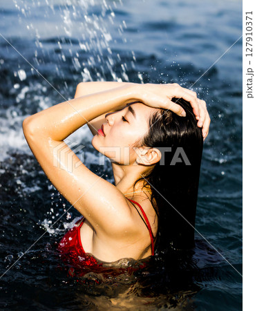 水しぶきがかかり、海で遊ぶビキニ水着の女性の写真 水しぶきがかかり、海で遊ぶビキニ水着の女性の写真 127910371