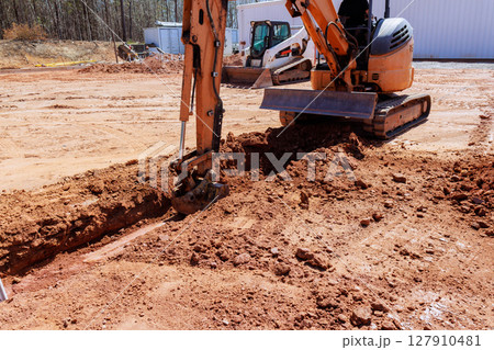 Heavy machinery is digs trench as workers prepare for construction location. 127910481