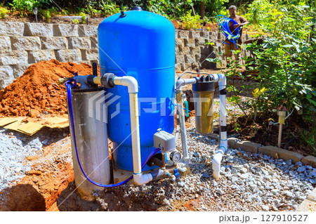 Workers set up artesian water well system in garden surrounded by gravel 127910527