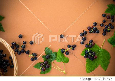 Scattered currant berries next to a basket on a brown background 127910757