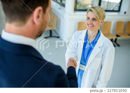 Doctor meeting pharmaceutical representative and shaking his hand, clinical setting. 127911030