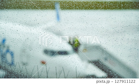 Rain falling on airport window blurs airplane and ground crew preparing for departure on a rainy day Rain falling on airport window blurs airplane and ground crew preparing for departure on a rainy day 127911122