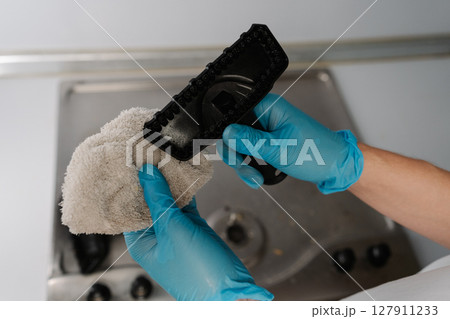 Close-up of unrecognizable man in gloves holding brush and microfiber cloth for steam cleaning dirty stainless steel gas stove, selecting best tool for sanitizing stainless steel stovetop surface. 127911233