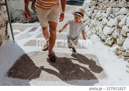 Close up on legs of father and toddler walking in town on summer holiday. 127911827