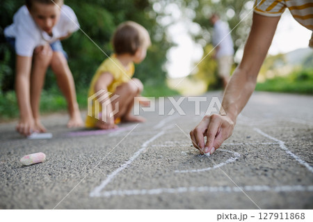 Mom and kids drawing with chalk on road. . 127911868