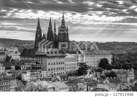 The first light of dawn casts a soft glow over Prague Castle, highlighting its majestic towers. The city awakens as sunlight breaks through the clouds, creating a magical atmosphere. 127911986