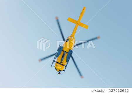Scenic bottom view modern yellow rescue emergency mountain helicopter flying against clear blue sky. Aviation transport machine silhouette alpine tourism service team 127912636