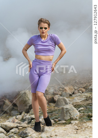 Sensuality woman fashion model with her eyes closed standing full length, sexy posing on rock in mountains. Geysers in crater of an active volcano release steam and gases, creating natural backdrop Sensuality woman fashion model with her eyes closed standing full length, sexy posing on rock in mountains. Geysers in crater of an active volcano release steam and gases, creating natural backdrop 127912643
