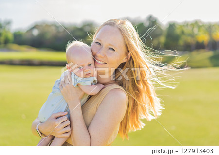 Mother and newborn baby on a meadow in the park. Tender bonding moment in nature. Parenthood, love, and family connection concept 127913403