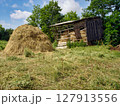 Countryside scenery with haystack among green grass meadow near old wooden hayloft barn at sunny summer day. With no people rural landscape, agricultural and country life theme. 127913556