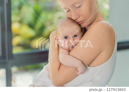 Mother gently hugging her baby at home, sharing a warm and loving moment. Parenthood, family bonding, and maternal love concept 127913603