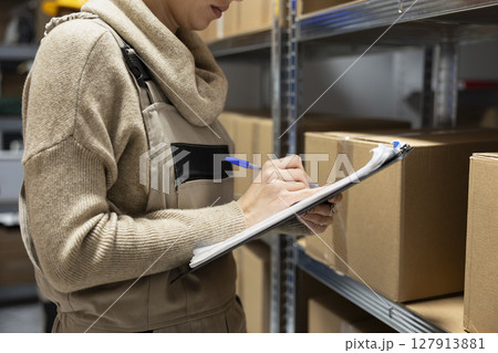 Industrial warehouse scene with employee counting merchandise to dispatch parcels. Shelving units filled with cargo highlight efficient logistics, delivery and inventory control operations. 127913881
