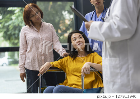 Healthcare medic supporting woman in wheelchair during routine appointment at inclusive clinic. Expert offering advice on maintaining wellness and adapting lifestyle around physical disability. Healthcare medic supporting woman in wheelchair during routine appointment at inclusive clinic. Expert offering advice on maintaining wellness and adapting lifestyle around physical disability. 127913940